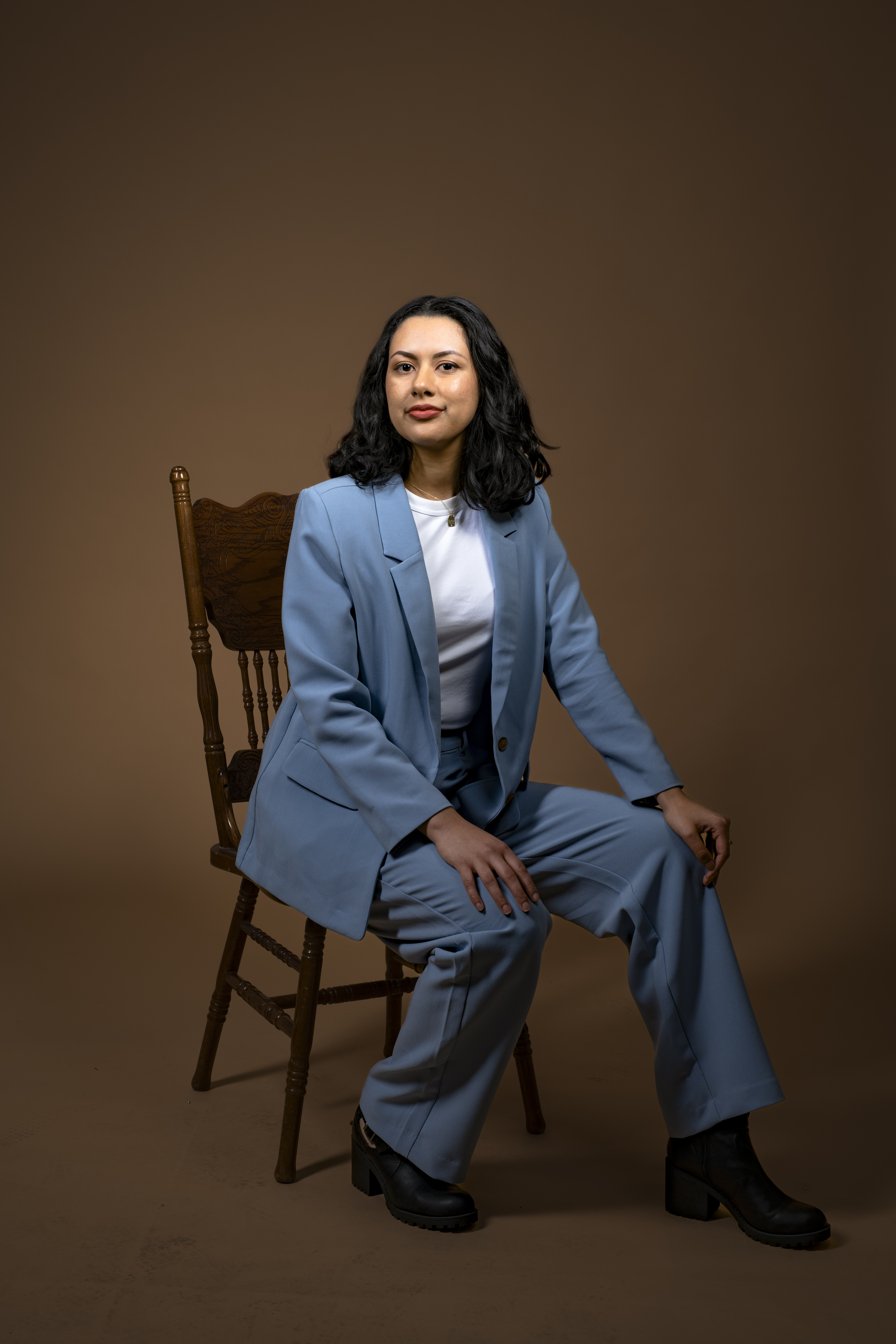 Self portrait of Therapist Dianne. She is dressed in professional attire while sitting on a wooden chair. 